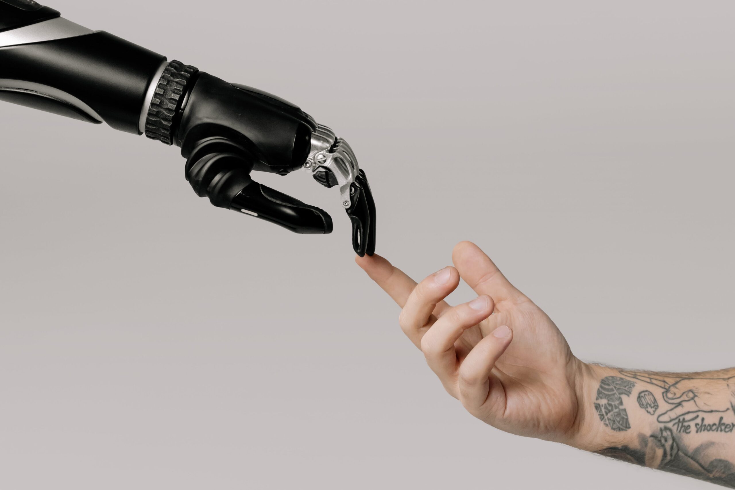A robotic hand and a human hand with tattoos about to touch fingers, reminiscent of Michelangelo's 'Creation of Adam', symbolizing the intersection of humanity and technology.